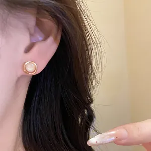 Elegant gold-tone round stud earring with white cat's eye stone shown on model's ear