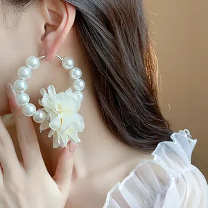 Dettaglio ravvicinato di eleganti orecchini a cerchio con perle e fiore in tessuto bianco.