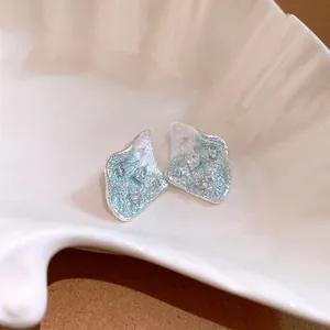 Close-up of pleated diamond earrings with blue texture and zircon accents in a shell