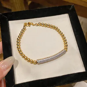 Close-up of elegant gold beaded bracelet with shimmering zircon curved bar detail.