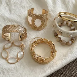 Detailed close-up of varied gold-tone geometric metal bangles and stone bracelets