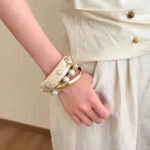 Detailed close-up of a stylish layered bracelet set with shell charms and gold bangles