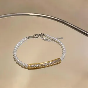 Elegant pearl bracelet with gold zircon bar on a reflective surface detail view.