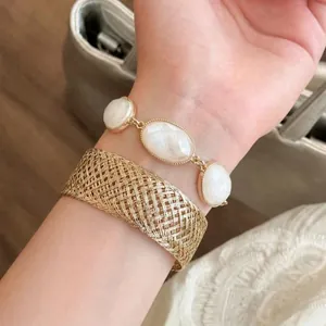 Detailed view of woven gold mesh bangle and oval white stone bracelet on wrist
