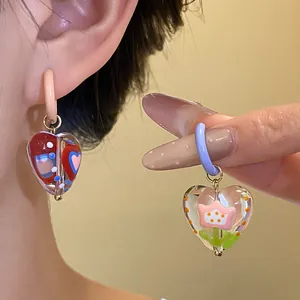 Close-up detail of colorful heart-shaped glass hoop earrings with flower patterns