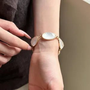Elegant gold-toned bracelet with oval translucent white stones on a woman's wrist.
