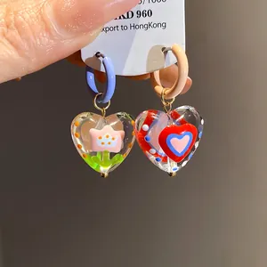 Close-up of sweet dopamine style glass heart earrings with flower and heart motifs.