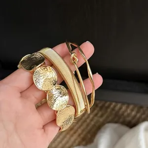 Elegant set of four gold-toned geometric bracelets with hammered textures and knotted details
