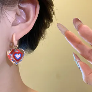 Macro view of sweet heart-shaped glass pendant earrings elegantly worn on the ear.