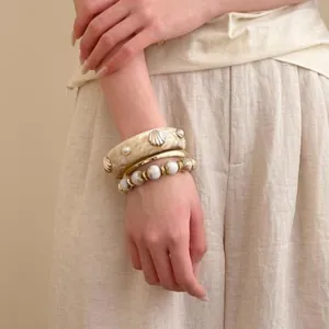 Close-up of stacked bracelets featuring a cream shell bangle and gold metal bands