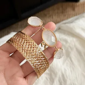 Detailed close-up of a golden mesh bangle and white oval stone bracelet held in hand