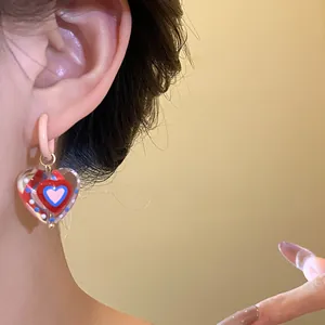 Close-up detail of sweet dopamine style glass heart pendant earrings worn on the ear.