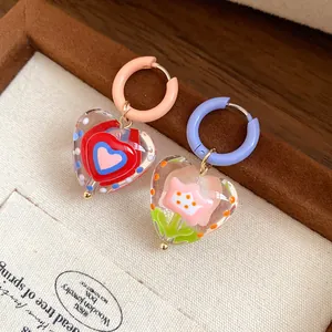 Close-up of glass heart earrings with colorful oil-drop flower and heart patterns