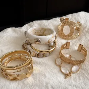 Detailed close-up view of gold geometric bracelet set with marble and shell accents on fabric