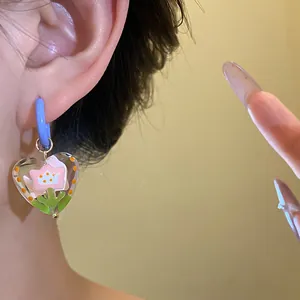 Close-up detail of sweet heart-shaped glass earring with pink flower and blue hoop charm.