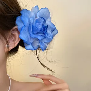 Close-up of large blue fabric flower hair clip with mesh petals worn by model.