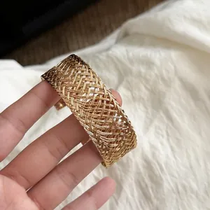 Detail view of a wide gold woven metal cuff bracelet with intricate lattice pattern.