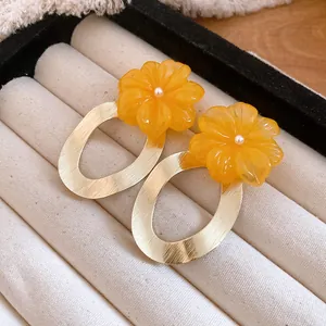 Primo piano di orecchini a fiore in resina con pendenti ovali in oro spazzolato