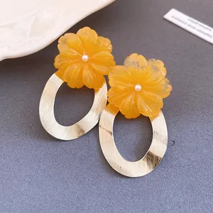 Dettaglio degli orecchini a fiore in resina gialla con pendenti ovali dorati spazzolati
