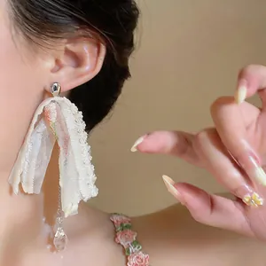 Close-up of a white lace flower earring with a crystal teardrop on a model's ear