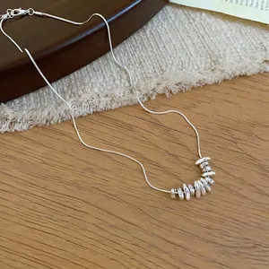 Elegant silver-colored necklace with irregular pebble pendants on a warm wood surface.