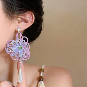 Gros plan sur les boucles d'oreilles fleurs perlées avec pampille en perle.