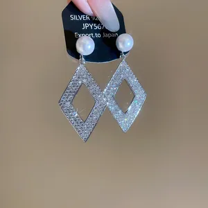 Detail of geometric rhombus earrings with sparkling stones and an elegant white pearl.