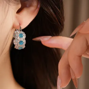 Detailed close-up view of a blue cat's eye and zirconia hoop earring worn on a model's ear.