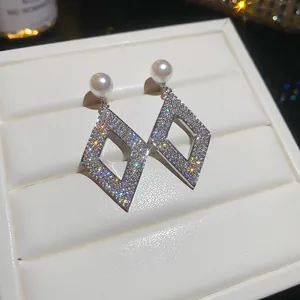 Close-up of sparkling geometric diamond-shaped earrings with elegant white pearls in box.