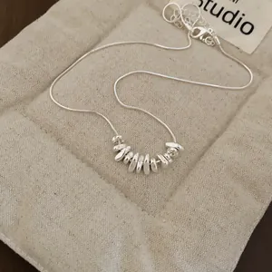 Close-up of a minimalist silver necklace with irregular pebble-shaped pendants on a soft pouch.
