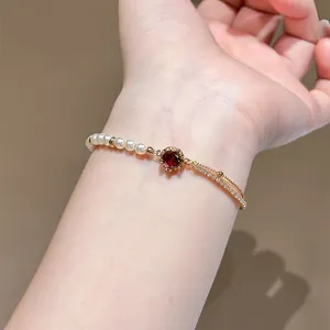 Close-up detail of 18K gold plated bracelet featuring red zircon and white pearls on a wrist