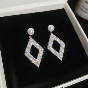 Macro shot of elegant geometric rhombus earrings featuring pavé crystals and white pearls