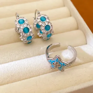 Close-up of blue cat's eye hoop earrings and star ring set in a cream jewelry box
