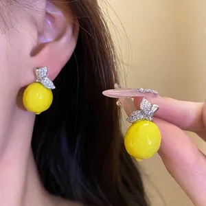 High-end zircon-encrusted yellow lemon pendant earrings displayed on a model's ear and hand