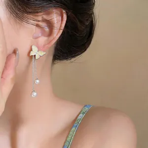 Detail of butterfly stud earrings with pearl tassels worn by a model in a forest style