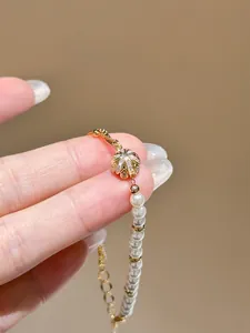 Detail view of elegant gold-plated flower charm with zircons on a delicate pearl bracelet