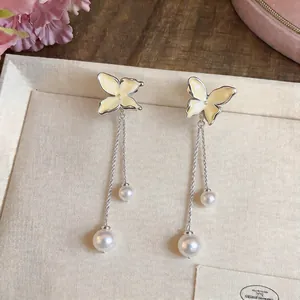 Detail of elegant silver needle earrings featuring enamel butterflies and dangling pearls.
