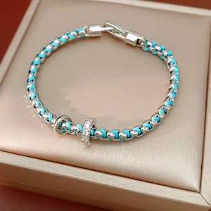 Detailansicht eines blau gewebten Armbands mit zirkonia-besetzten Anhängern auf Box