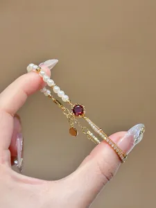 Close-up of elegant 18K gold plated bracelet featuring pearls and red zircon stones