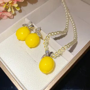 Close-up view of a pearl beaded necklace and earrings set featuring yellow lemon pendants