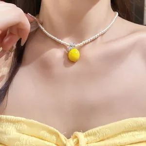 Detailed view of a pearl necklace with a sparkling zircon lemon pendant on a model.