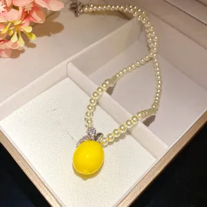 Close-up of pearl beaded necklace featuring a vibrant yellow lemon pendant with zircon leaves