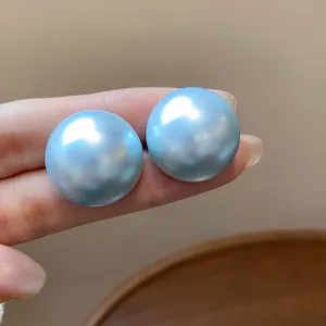 Primer plano detallado de pendientes de perlas azul claro irisadas para escala.