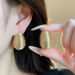 Minimalist gold oval earrings with horizontal texture shown on ear and held by hand