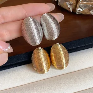 Minimalist textured oval stud earrings in silver and gold tones on a display stand
