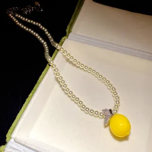 Macro view of a pearl necklace featuring a vibrant yellow lemon pendant with zircon leaves