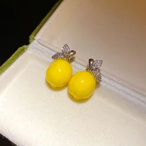 Macro detail of yellow lemon-shaped earrings with sparkling zircon leaves in a box