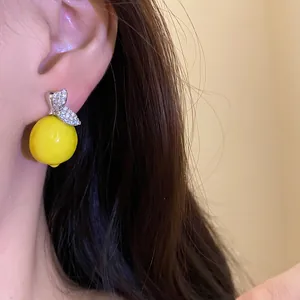 Detailed view of a yellow lemon-shaped drop earring with sparkling zircon leaves on a model.