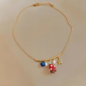 Detailed close-up of a gold chain necklace featuring strawberry, star and pearl charms
