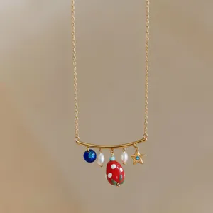 Detail view of a gold necklace with star, pearl, and red drip oil strawberry pendant charms.
